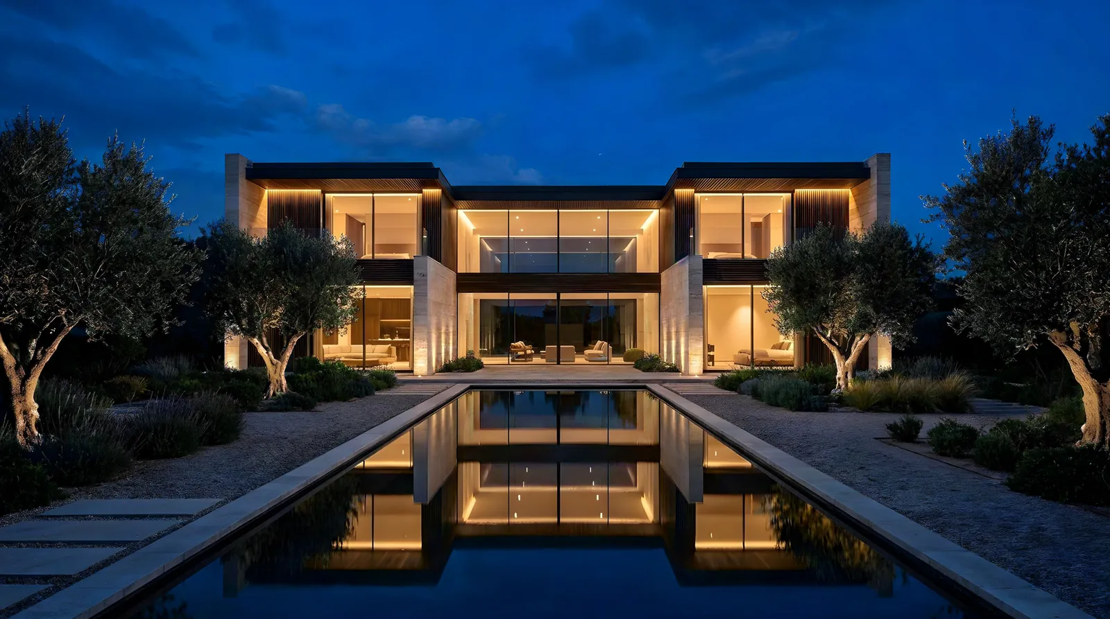 Dieselbe Villa, alle Fenster leuchten warm, Bodenstrahler beleuchten Steinwände und Olivenbäume, das Licht spiegelt sich im Pool.