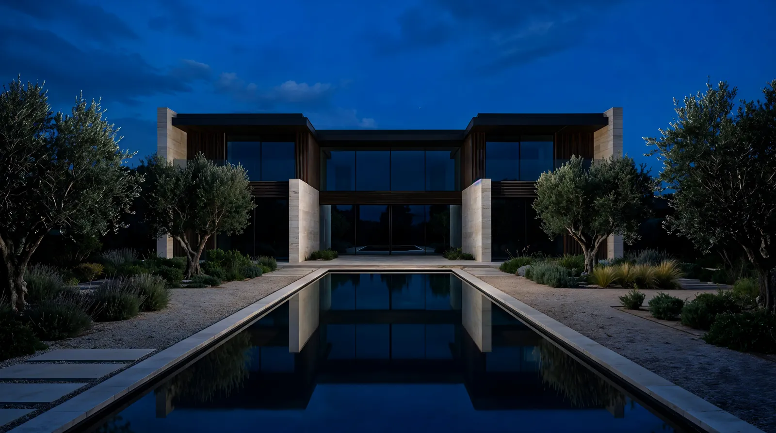 Moderne Villa aus Travertin und dunklem Holz zur blauen Stunde, davor ein langer spiegelnder Pool und Olivenbäume, alle Lichter aus.